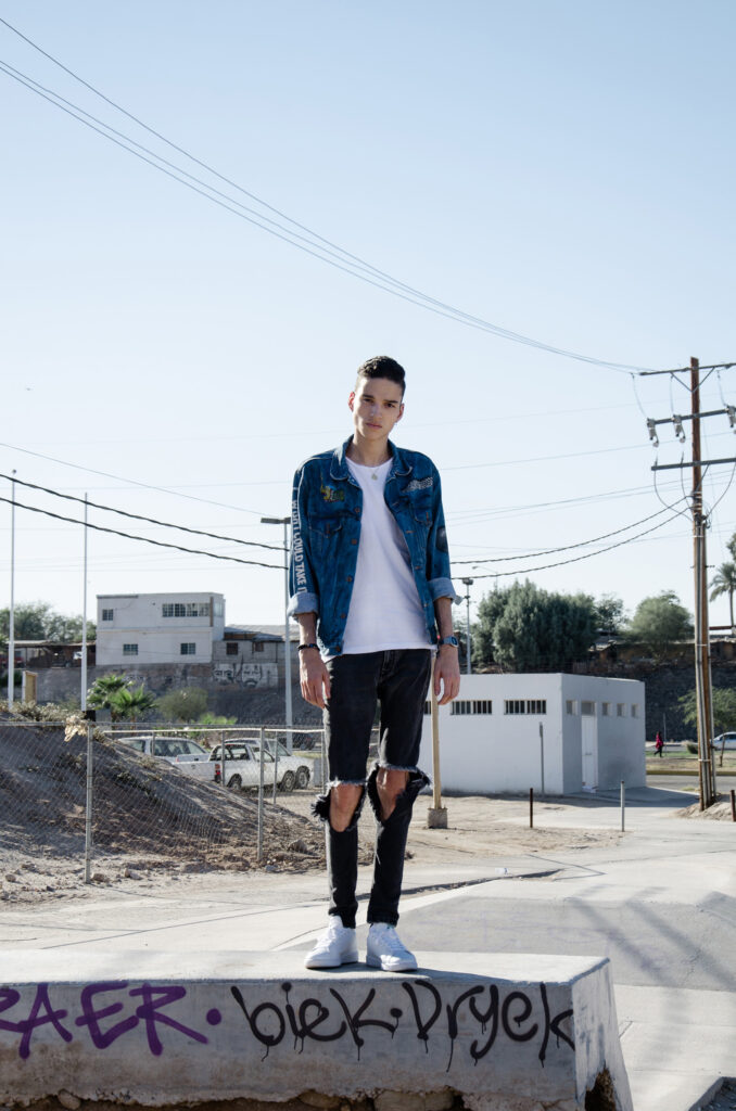 Victor Zepeda stands confidently on a concrete block surrounded by an urban setting with graffiti power lines." and buildings.